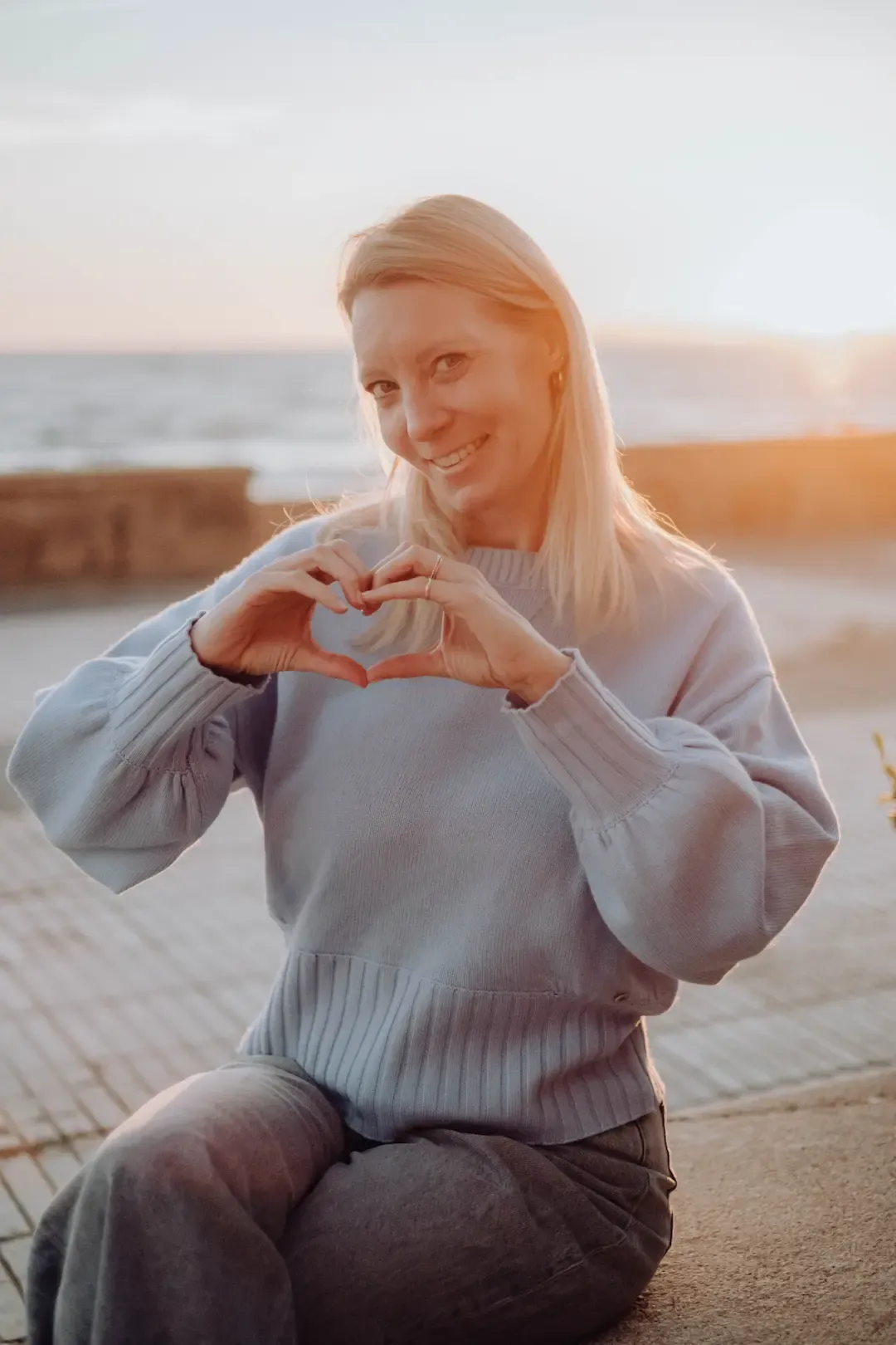Nadine Kleifges formt mit ihren Händen ein Herz, im Hintergrund das Meer
