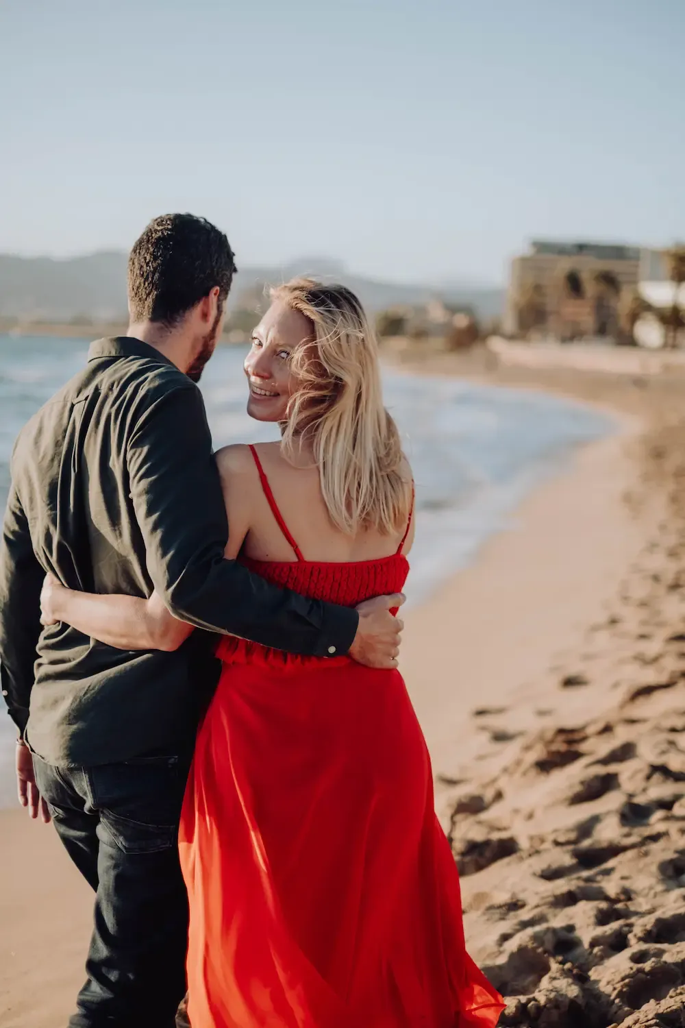 Nadine Kleifges in rotem Kleid, Arm in Arm mit ihrem Partner am Strand